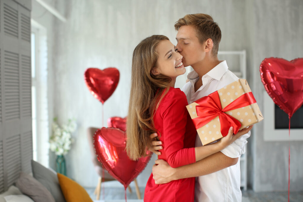 Jeune couple avec un coffret cadeau enlacé à la maison