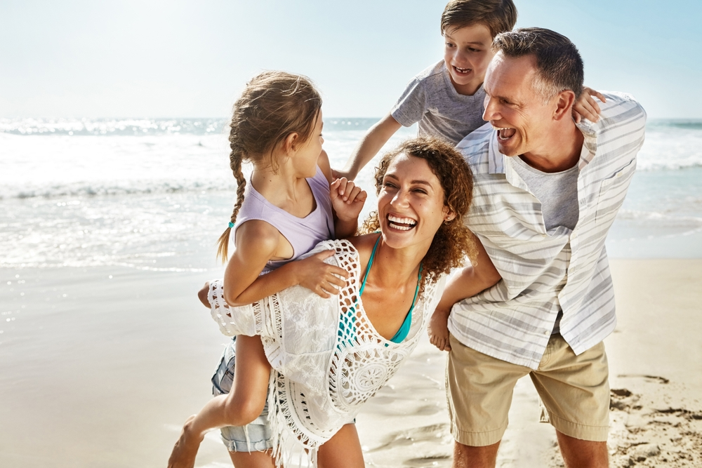 Une famille heureuse, riant sur la plage en été pour se détendre, voyager et passer des vacances en famille. 