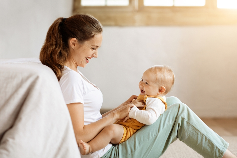 Jeune maman caucasienne tenant son bébé dans les bras et qui embrasse son adorable petit garçon, posant ensemble à la maison. 