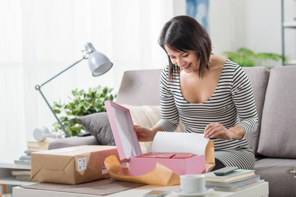 Femme heureuse et excitée à la maison, elle a reçu un colis postal et elle déballe son cadeau de fête des mères à distance.