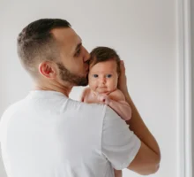 Jeune père barbu portant son nouveau-né, une petite fille, sur l'épaule.