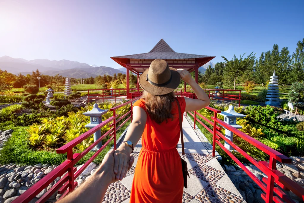 Femme en robe orange et chapeau tenant un homme par la main se rendant au jardin japonais avec une pagode.