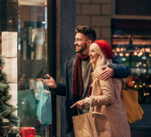 Vue de face d'un couple faisant des achats de noel pendant le black friday. L'homme adulte a son bras autour de la femme adulte et ils parlent de ce qu'il y a dans la vitrine.