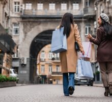 Vue arrière pleine longueur de photo d'amies sorties faire du shopping dans la ville. Deux copines marchant ensemble avec des sacs, achetant des vêtements le Black Friday.