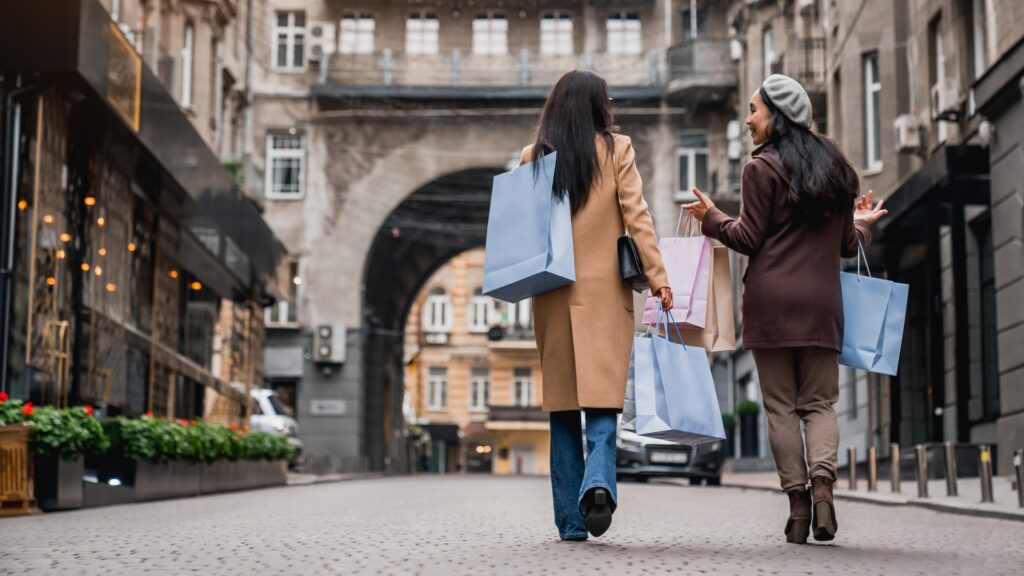 Vue arrière sur deux amies sorties faire du shopping en ville. Deux copines marchant ensemble avec des sacs, achetant des cadeaux au moment du black friday.