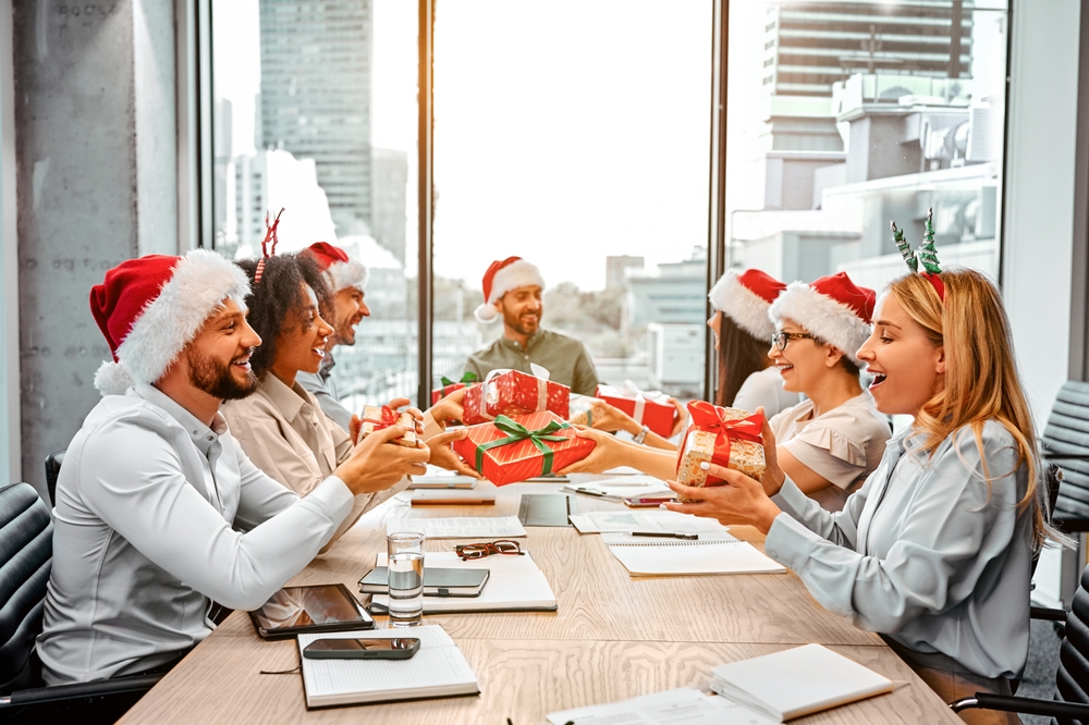 Échange de cadeaux secret santa au travail. Un groupe de collègues heureux sont assis à une table et échangent des cadeaux. Le Père Noël secret.