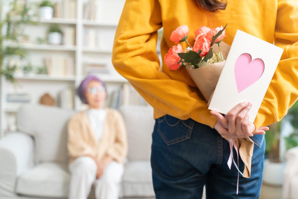 Une jeune fille heureuse pour la fête des mères présentant un bouquet de fleurs et une carte à sa mère âgée heureuse, à la maison ensemble.