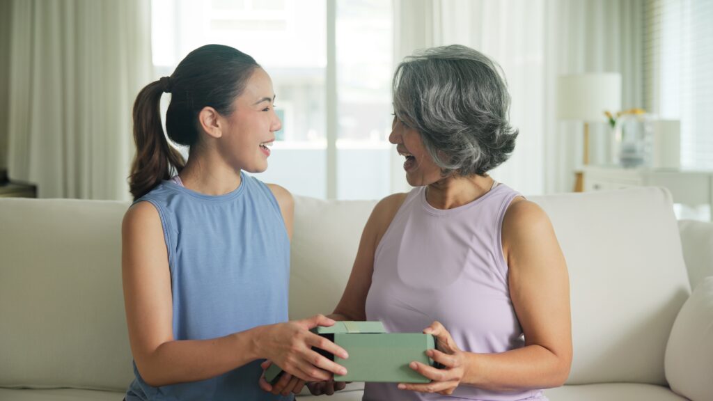 Une femme offre un cadeau à sa belle-mère à l'occasion de la fête des mères, assisent sur un canapé à la maison.