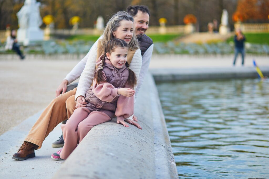 Famille heureuse de trois, père, mère et fille jouissant d'un temps en famille ensemble dans le jardin luxembourgeois de Paris, France.
