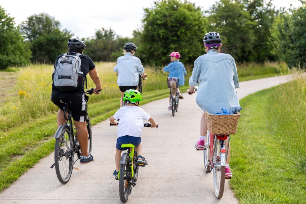 Une famille faisant du vélo à l'occasion de la fête des pères, pavé chemin de campagne vert prés arbres pendant la lumière chaude de jour d'été en Suisse.