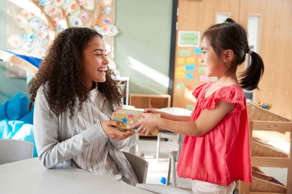 Une écolière de maternelle faisant un cadeau à sa maîtresse dans une salle de classe, vue latérale, gros plan.