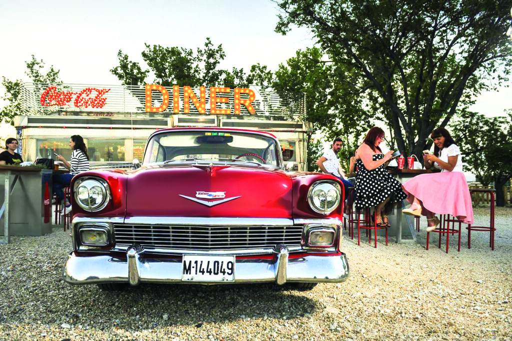 Coche clásico aparcado delante de un food truck y unas mesas con clientes