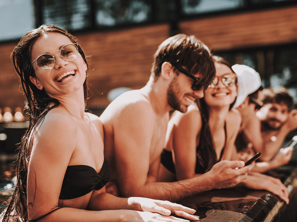 Grupo de amigos de vacaciones en fila en el poyete de una piscina