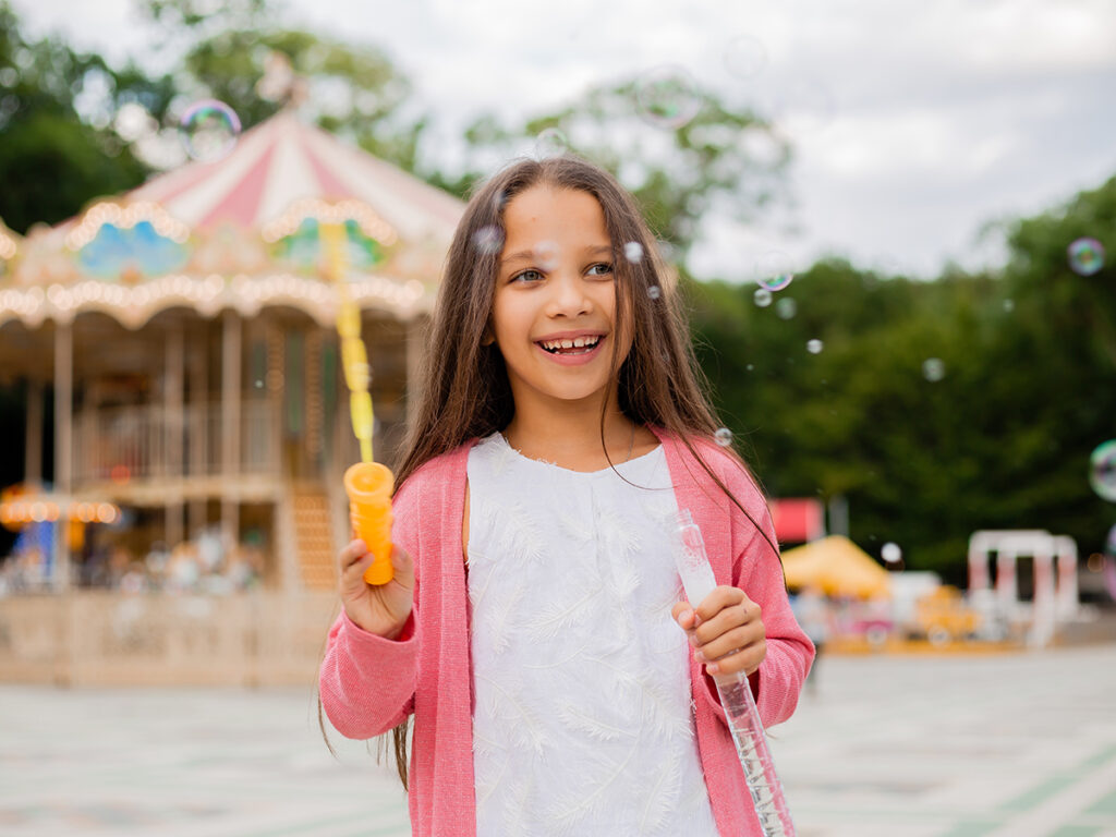 Niña en parque de atracciones soplando pompas