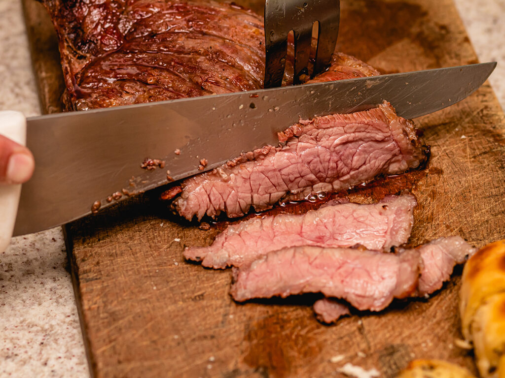 Una persona cortando carne a la barbacoa en una tabla de madera