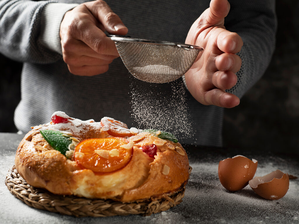 Persona espolvoreando azúcar en un roscón de reyes