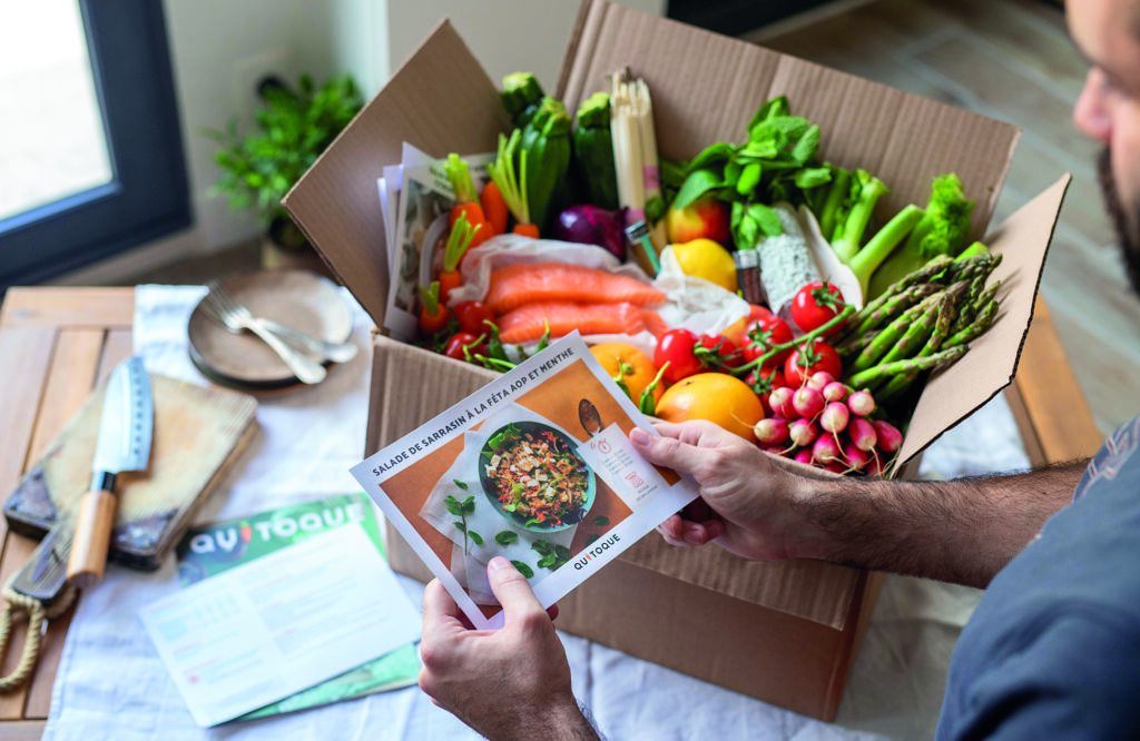 Boîte avec ingrédients pour cuisiner et homme lisant une recette