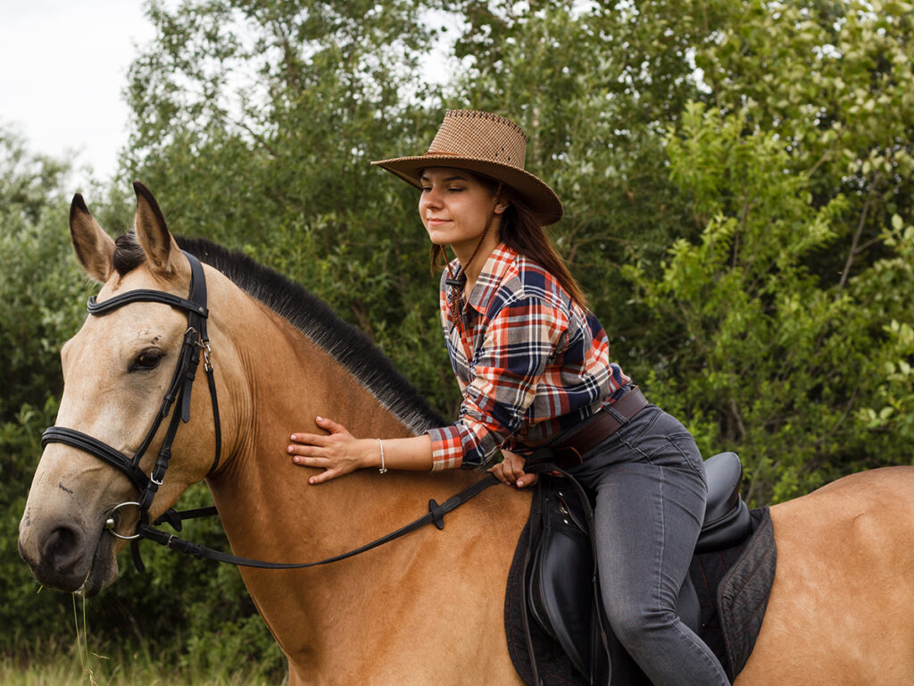 Jeune femme sur un cheval marron devant des arbres