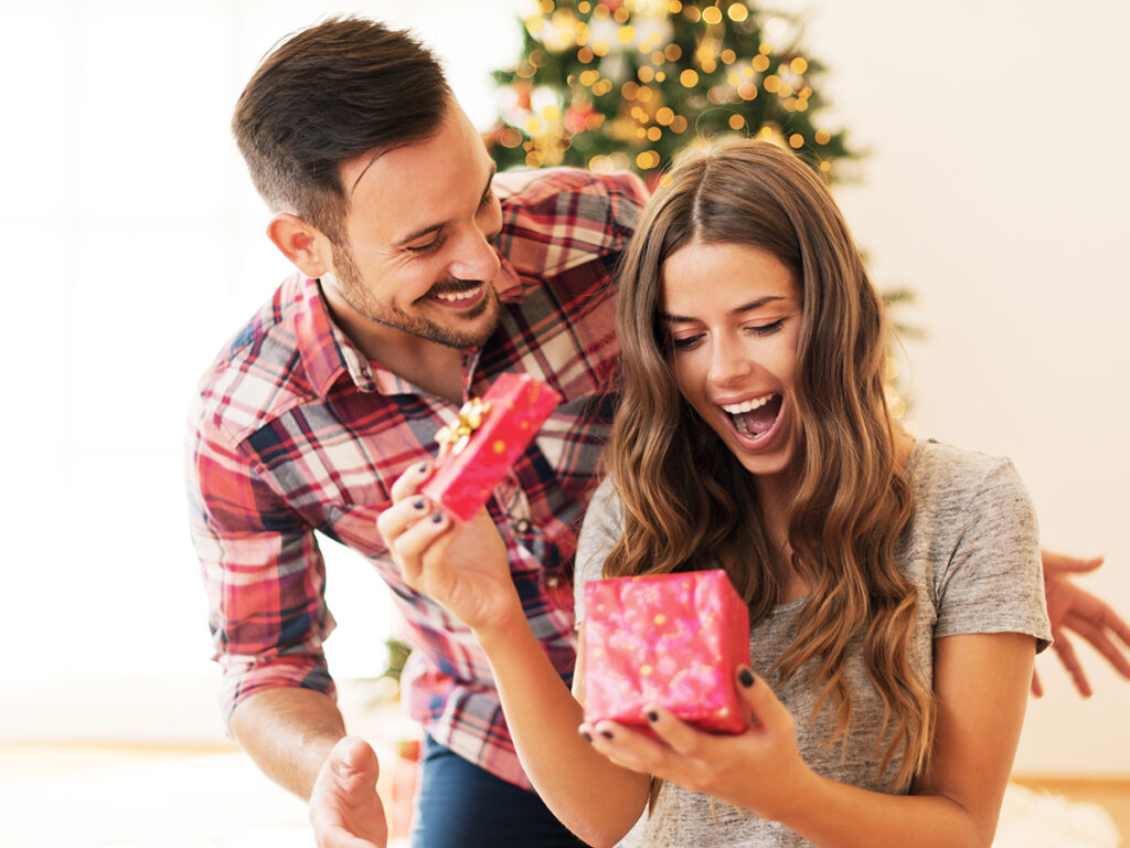 Jeune couple avec une jeune femme qui ouvre un cadeau l’air étonné